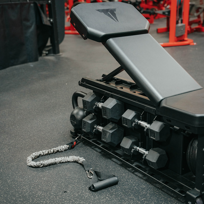SMTF FXD Bench with Accessories. Includes medicine ball, dumbbells, and kettlebells. Attachments for resistance tubes and other equipment at base of bench. 