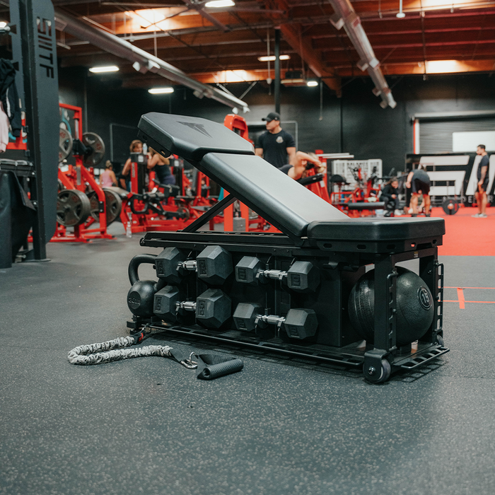 SMTF FXD Bench with Accessories. Includes medicine ball, dumbbells, and kettlebells. Attachments for resistance tubes and other equipment at base of bench. Easy to fit in existing gym space.